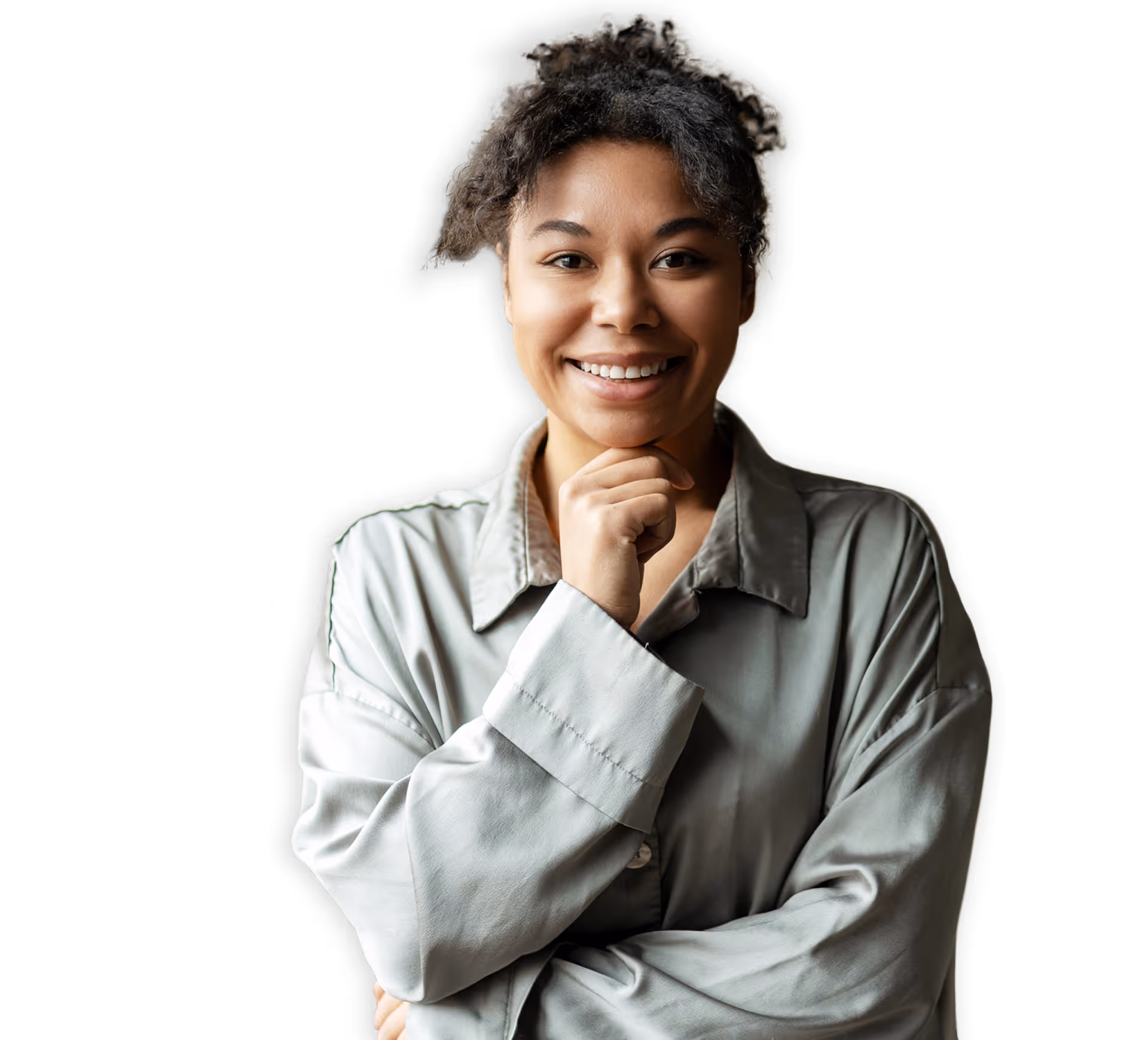 Jeune femme souriante avec les cheveux bouclés, portant une chemise grise, posant avec une main sous le menton sur fond noir.