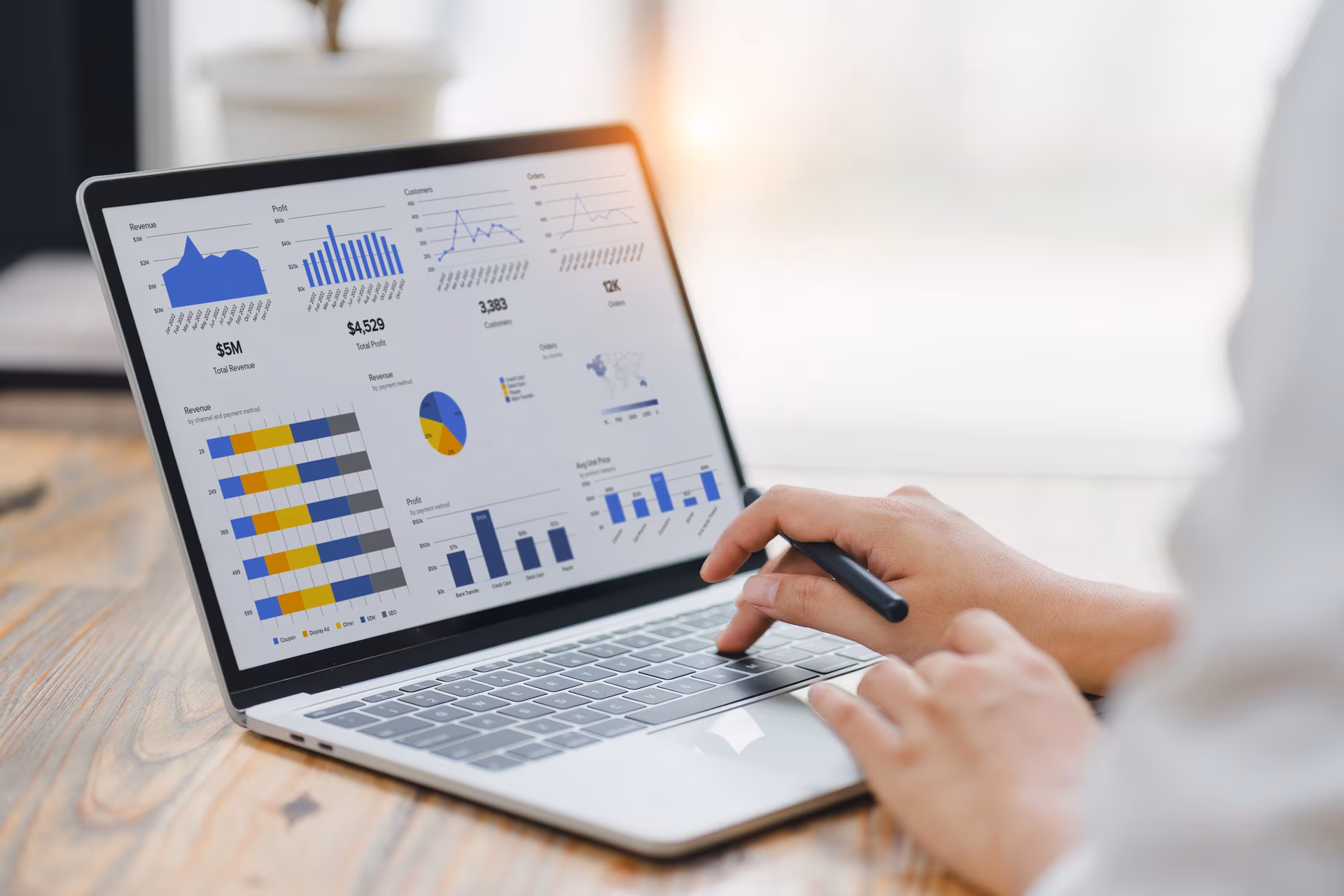 Une personne utilise un ordinateur portable affichant plusieurs graphiques et diagrammes financiers colorés sur un bureau en bois.