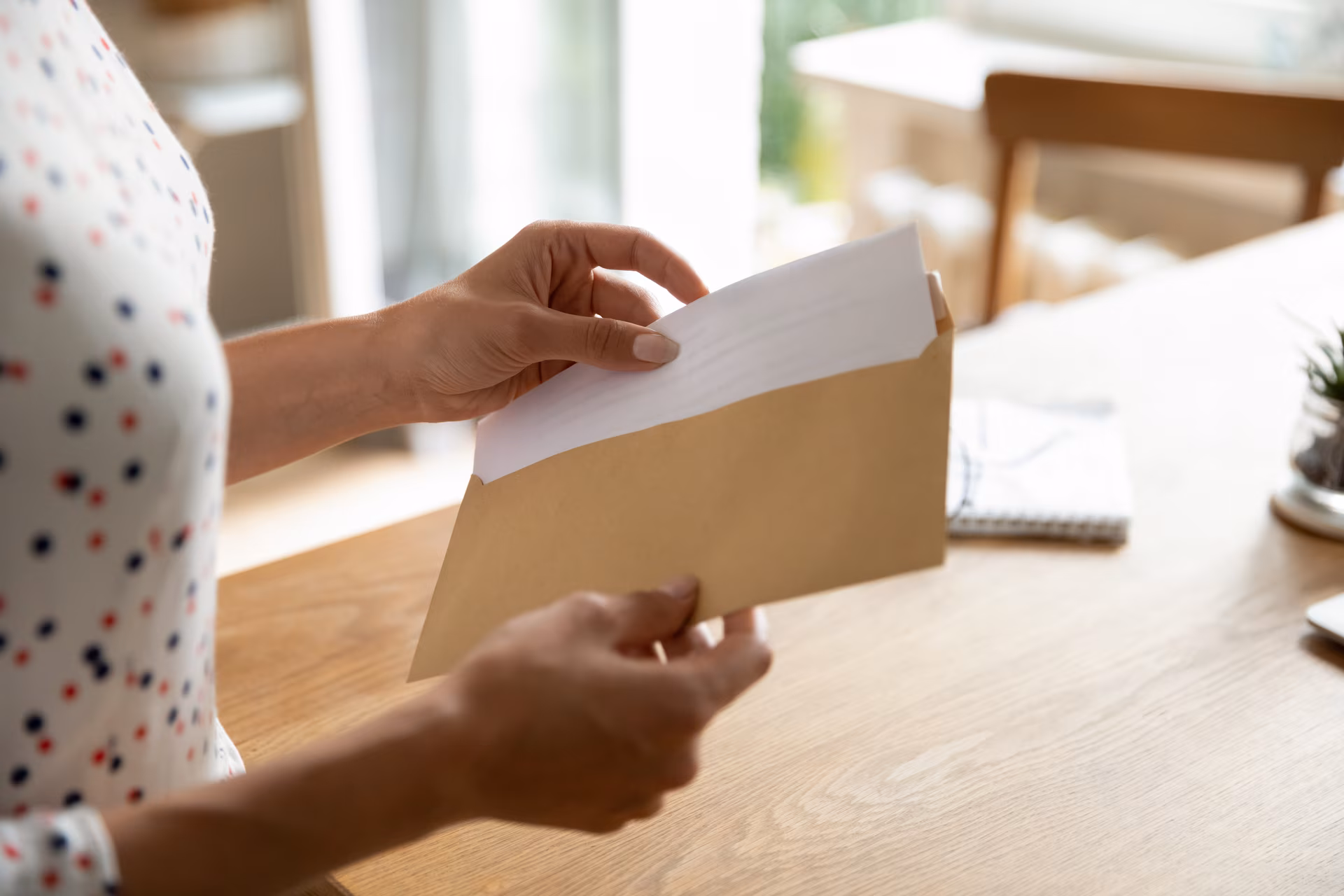 Une personne tenant une enveloppe brune et en retirant une feuille blanche à l'intérieur au-dessus d'une table en bois.
